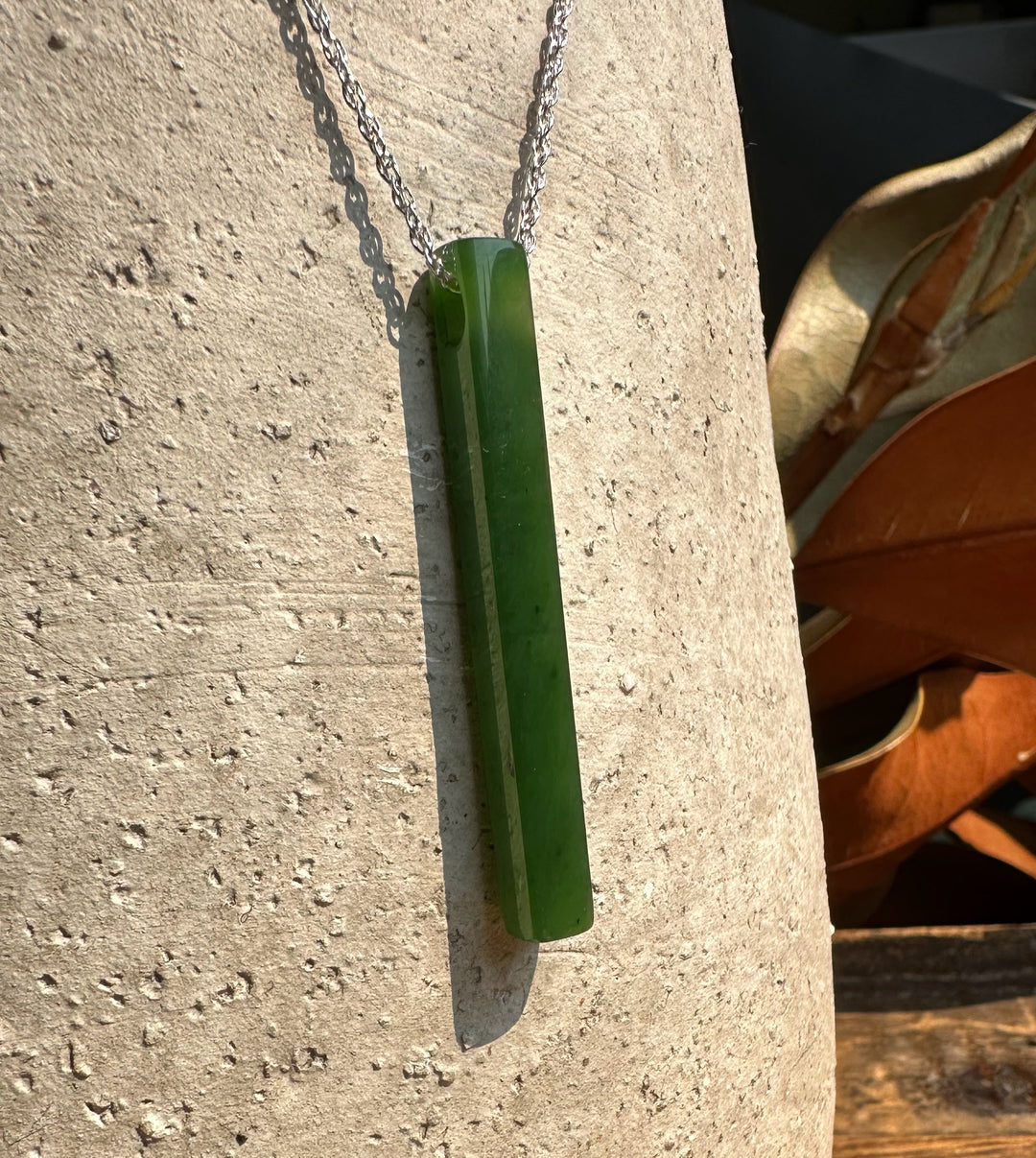 1.75 inch slender green jade pendant on a silver chain against a light stone background