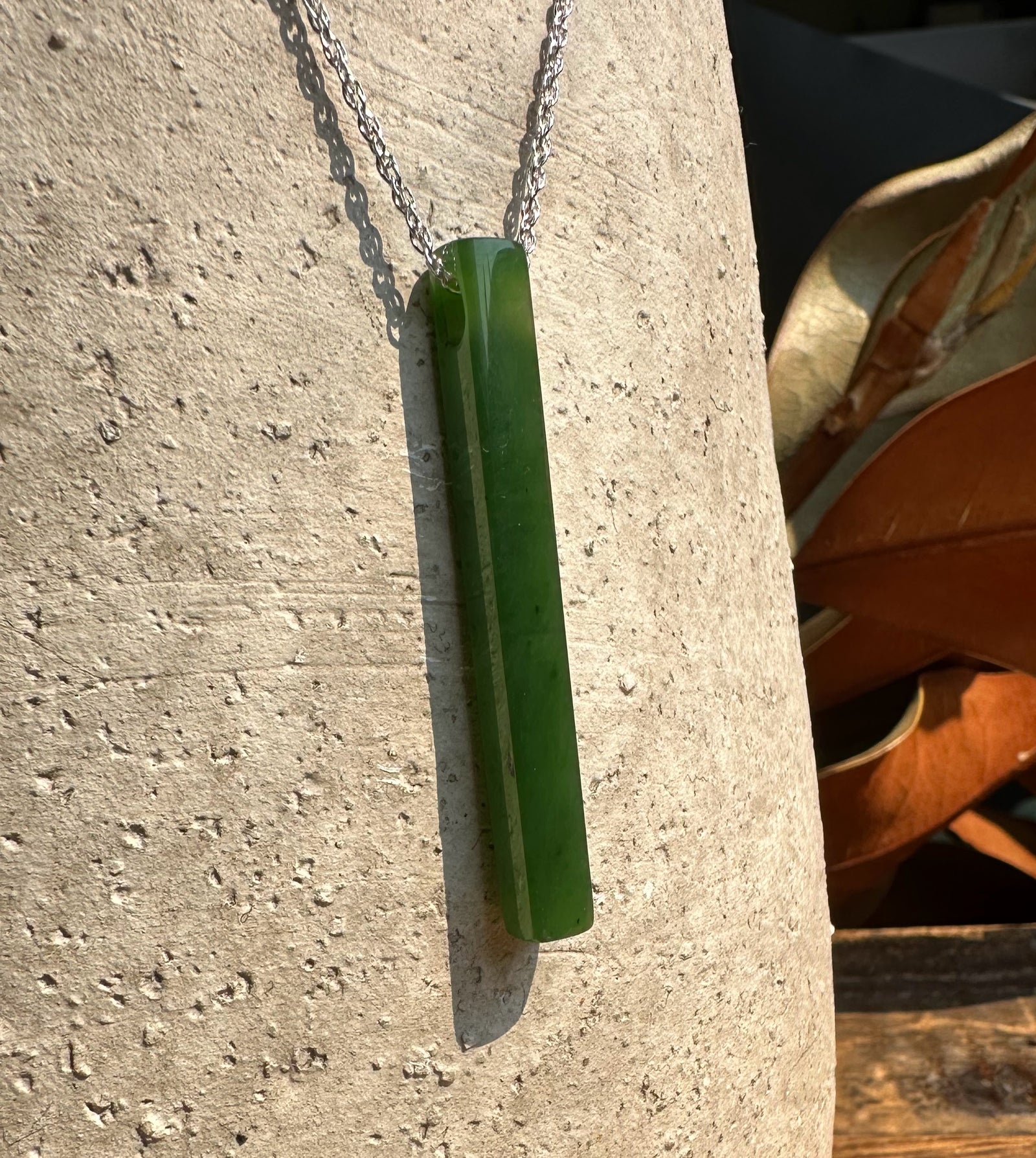 1.75 inch slender green jade pendant on a silver chain against a light stone background