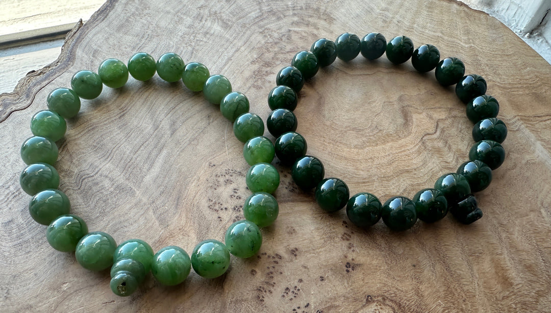 Dark green and medium green bead bracelet beside each other on a wooden base