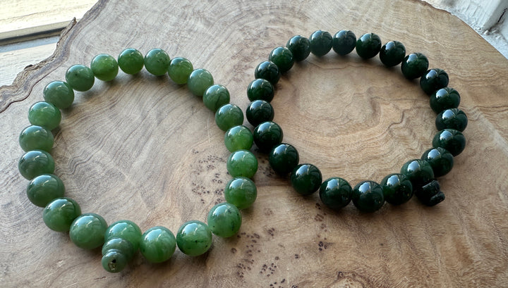 Dark green and medium green bead bracelet beside each other on a wooden base