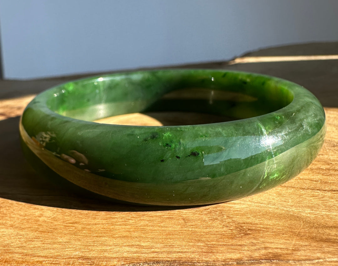 Canadian Jade Bangle 60.5 x 15.5mm green jade on a wooden surface with a blue background