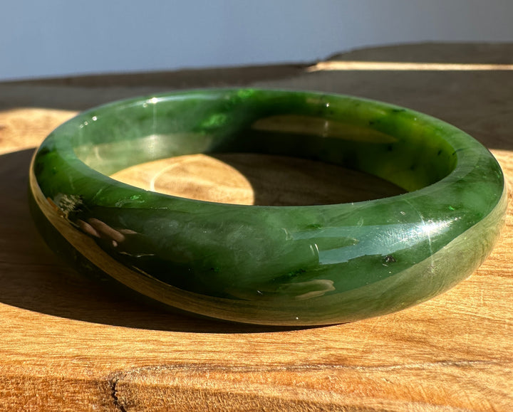Canadian Jade Bangle in deep green resting on a wooden surface.