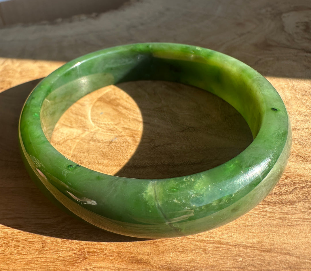 Canadian Jade Bangle 60.5 x 15.5mm close up of green jade with dark inclusions and shine