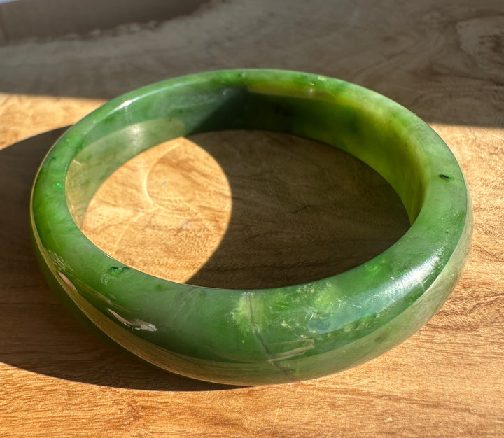 Canadian Jade Bangle 60.5 x 15.5mm close up of green jade with dark inclusions and shine