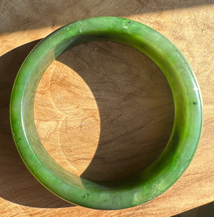 Top view of a green jade bangle on wood with the inner opening visible.