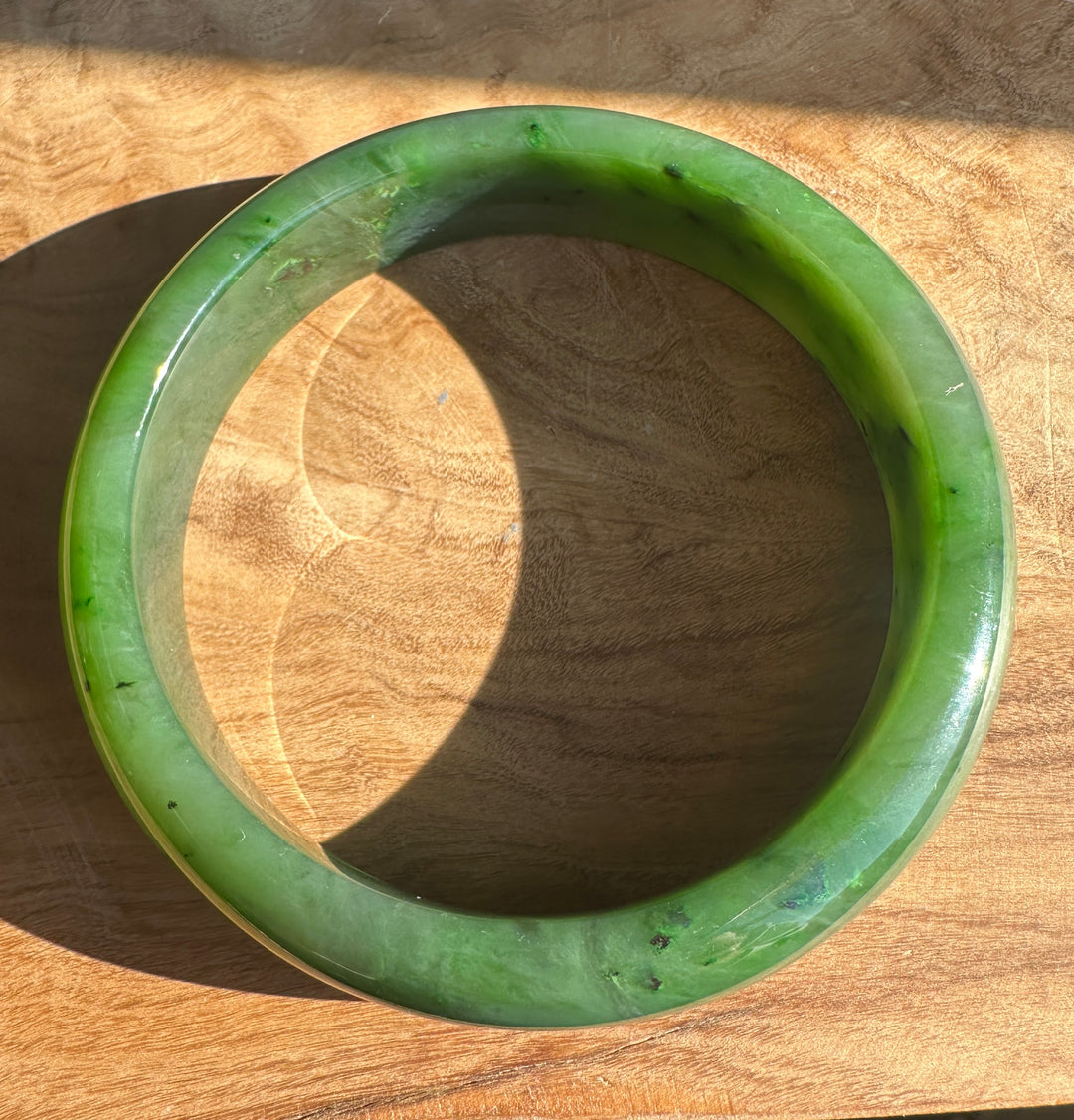 Glossy green Canadian jade bangle resting on a wooden surface