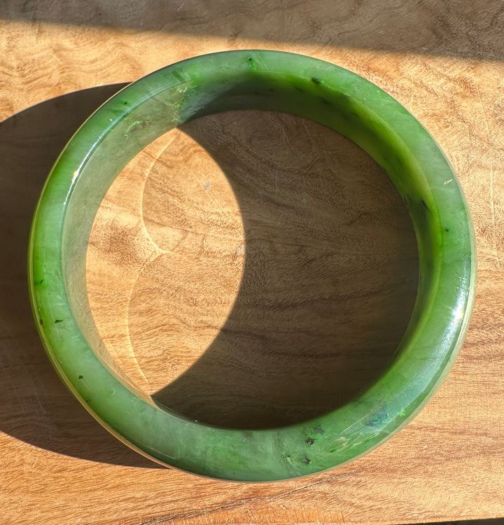 Glossy green Canadian jade bangle resting on a wooden surface