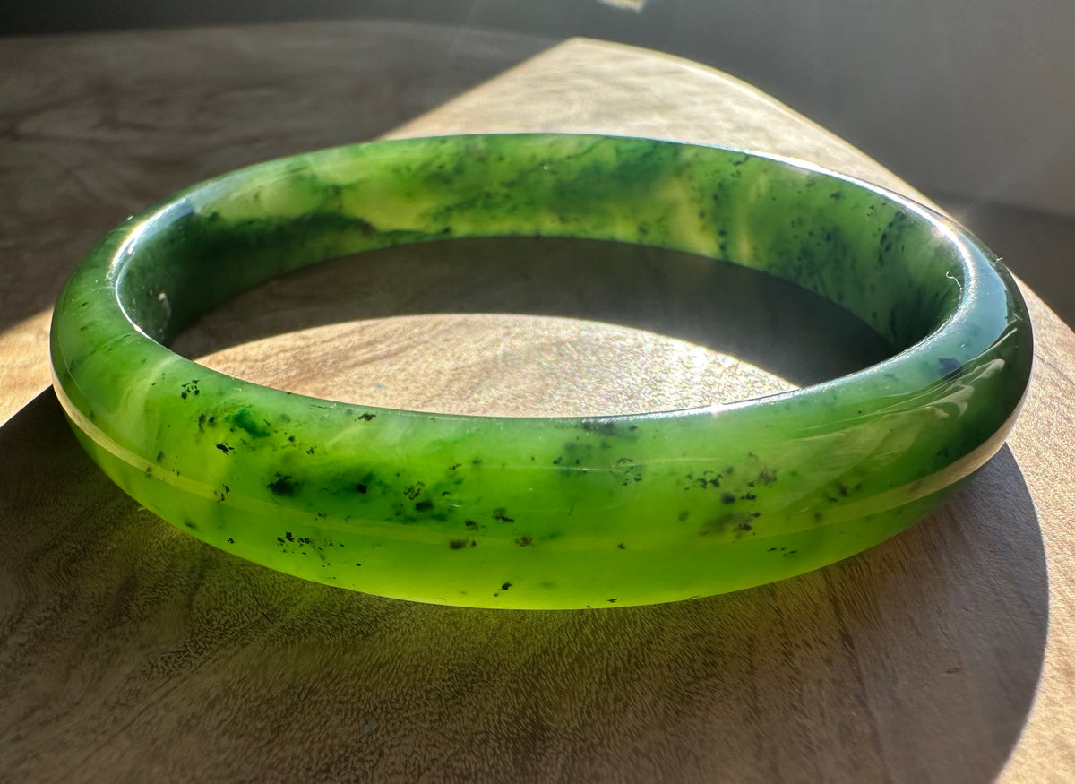 Inner side of a bright green jade bangle with marbled pattern resting on wood