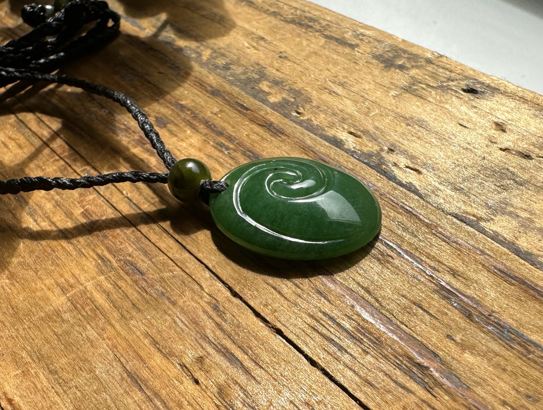 Green jade pendant with circular spiral carving on a wooden surface attached to a black cord