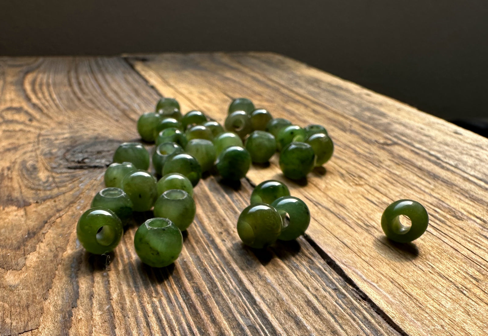 Group of 8mm green jade beads with large holes on a wood surface with one bead in the foreground