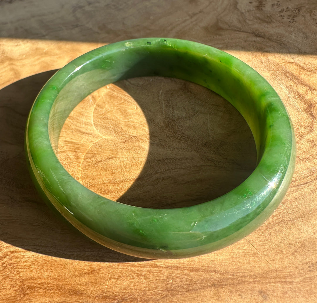 Close-up of a smooth green jade bangle on a wooden background.
