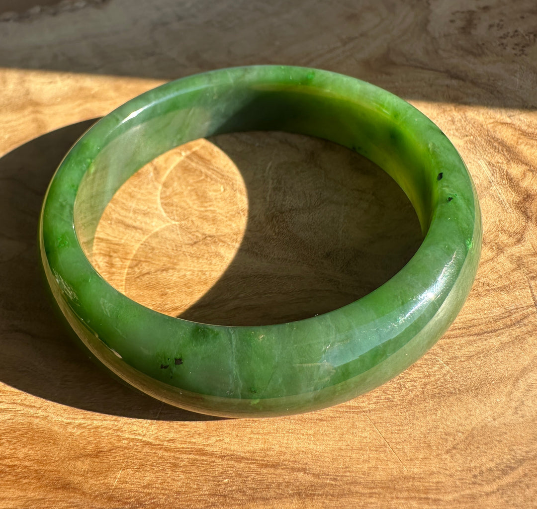Bright green jade bangle resting on a wooden surface under warm light.