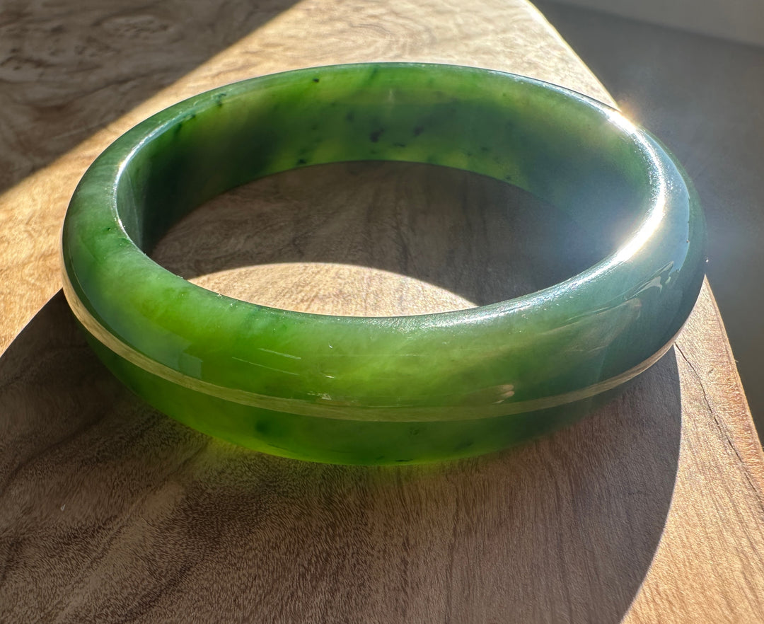 Green jade bangle with sunlit edge on a wooden surface.