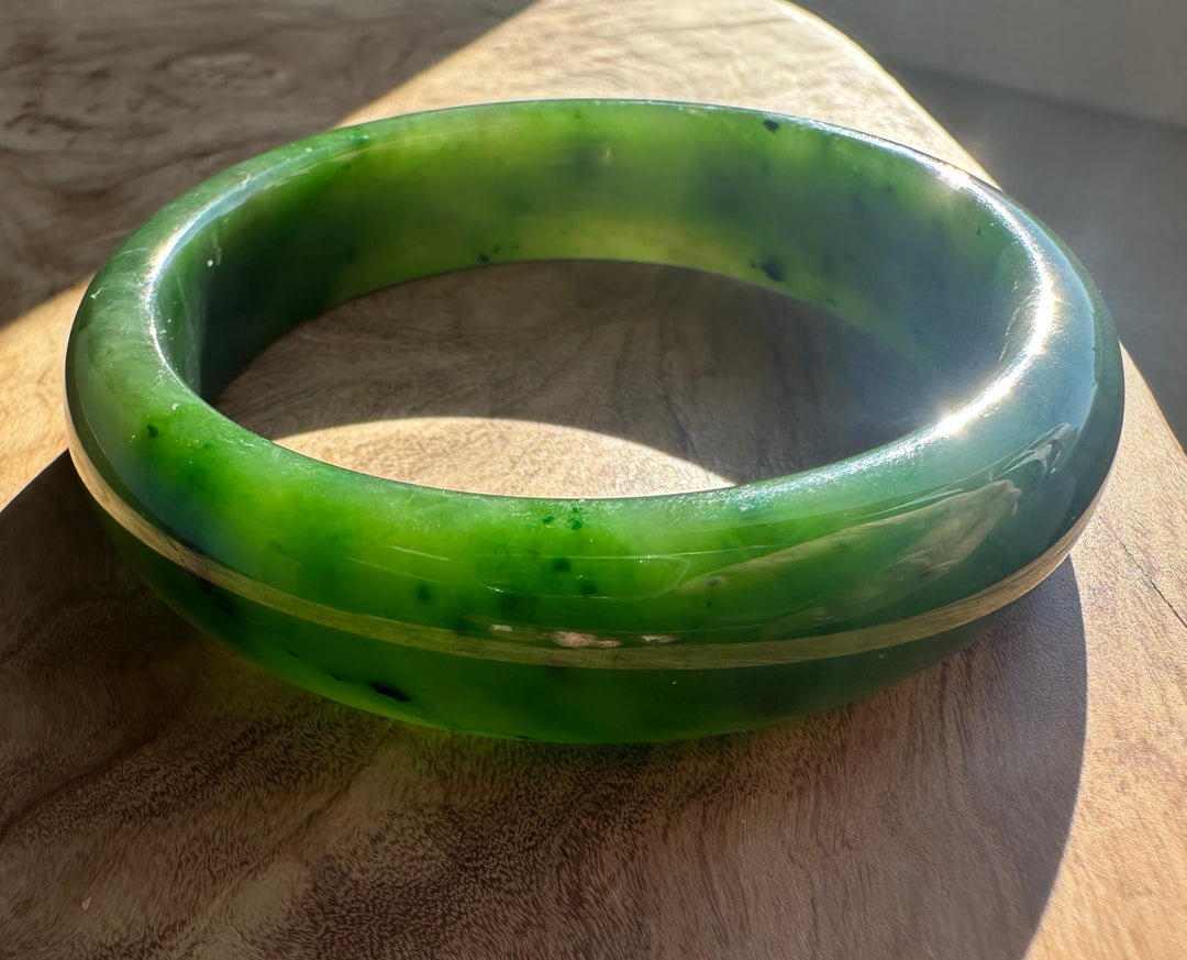 Close up of a bright green jade bangle resting on a wooden surface in sunlight