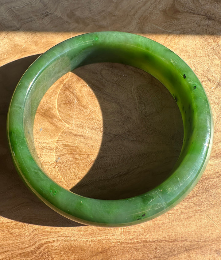 Top-down view of a jade bangle curved on a wooden table.