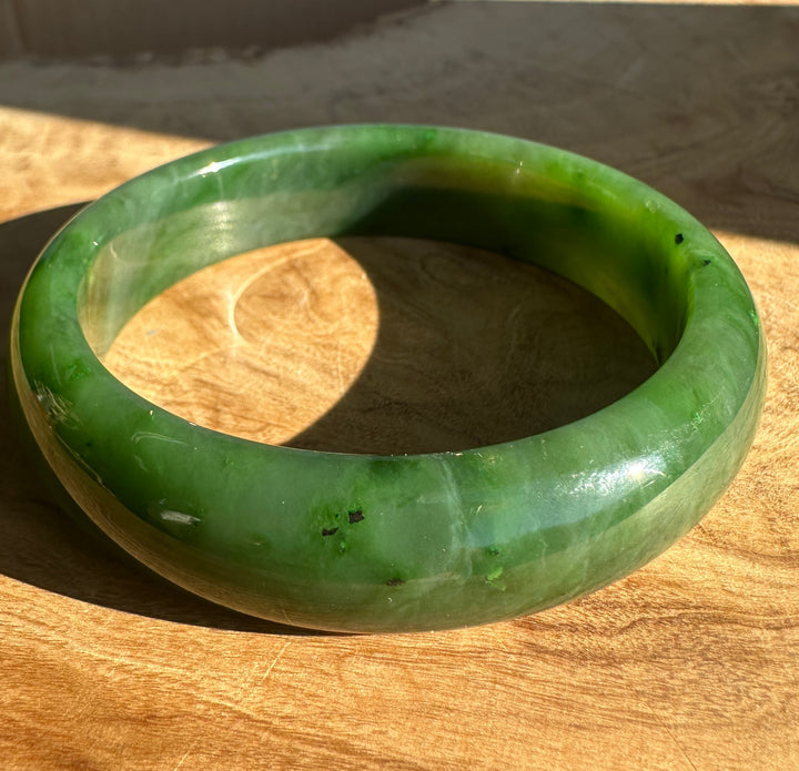 Glossy emerald green jade bangle resting on a wooden surface.
