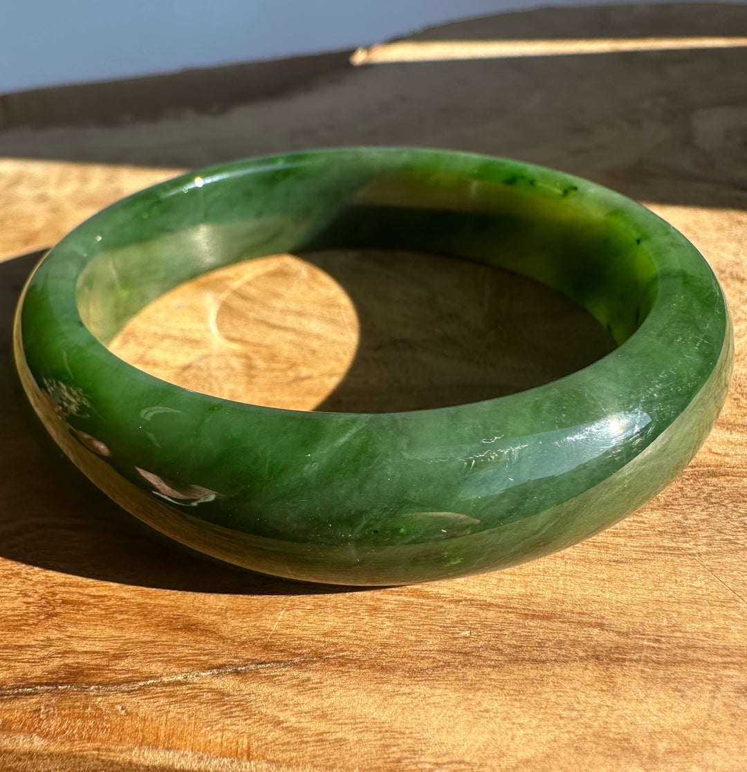Wrist shot of a glossy green jade bangle with subtle dark inclusions