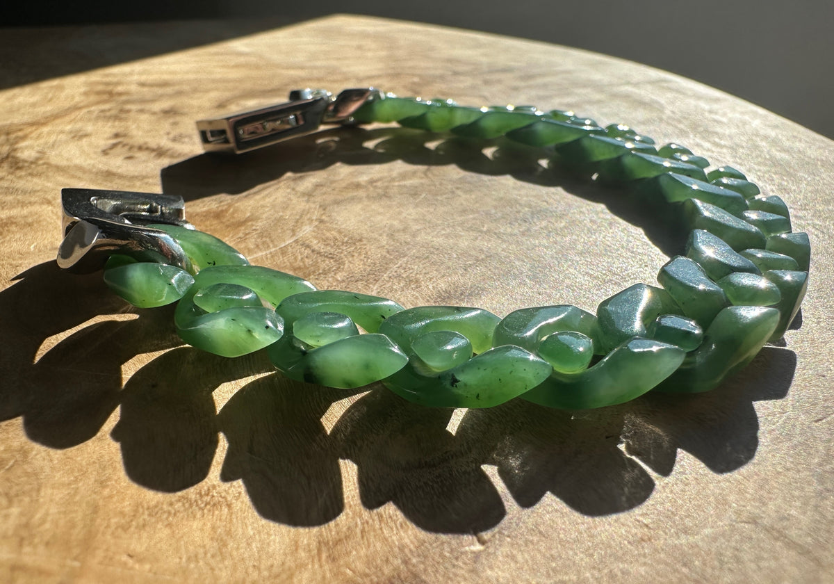 Side view of the green nephrite Cuban link bracelet with silver clasp resting on a wooden surface