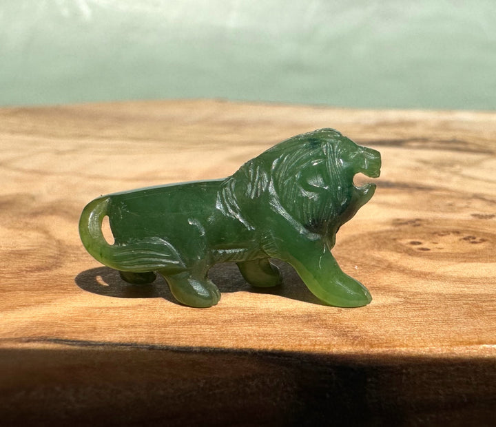 Small jade lion figurine on a wooden surface, about 1 inch tall