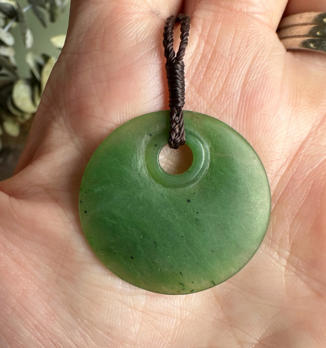 Close-up of jade round pendant 30mm on a braided brown cord held in a hand.