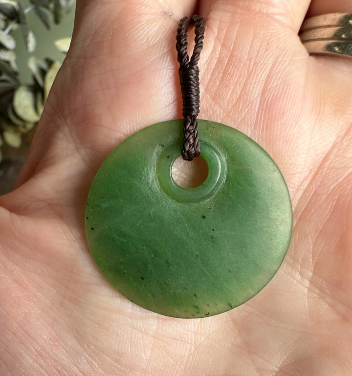 Close-up of jade round pendant 30mm on a braided brown cord held in a hand.