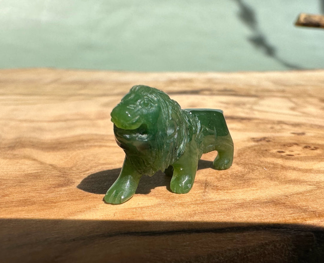Side profile of a green jade lion figurine with an open mouth on a wooden surface