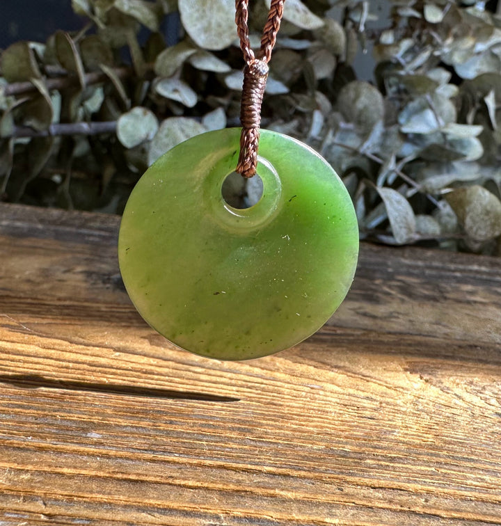 Round green jade pendant with a central hole on a brown braided cord