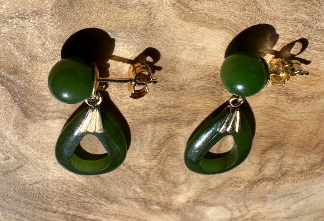Two green jade drop earrings laid on wood showing round studs and hollow teardrop pendants