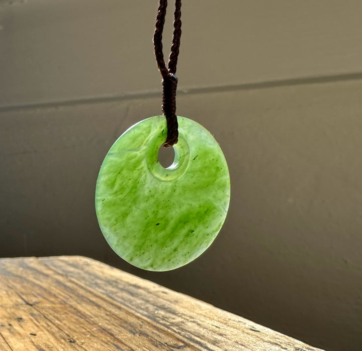 Green circular jade pendant with a central hole suspended from a twisted silver chain