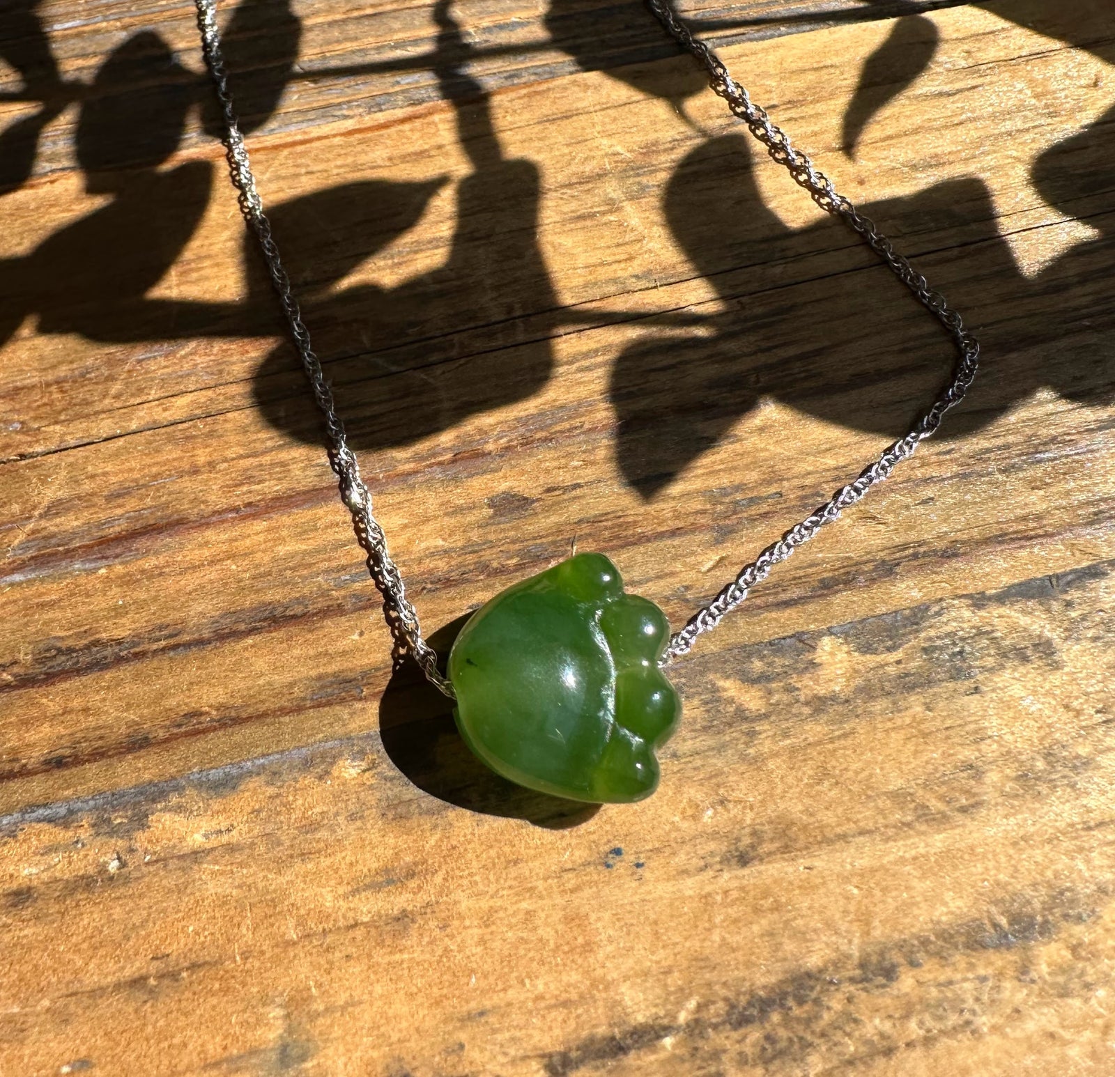 Jade cat paw pendant on a silver chain resting on a wooden surface