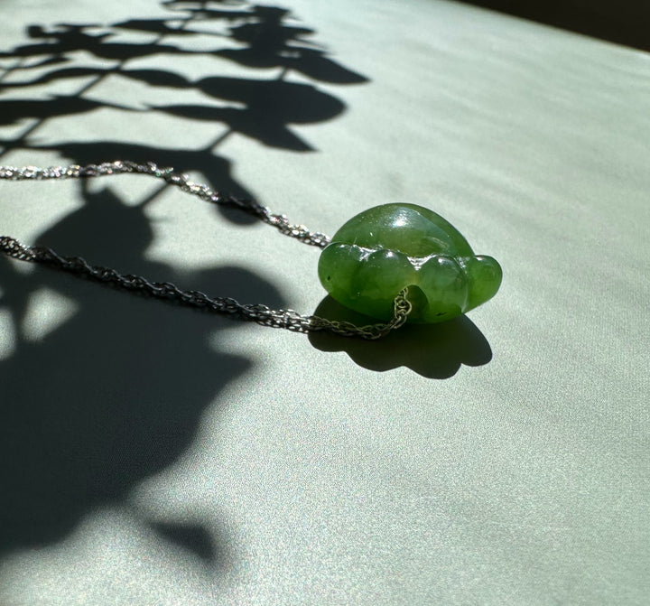 Close up of jade cat paw pendant on a silver chain with leaf shadows on a light green surface