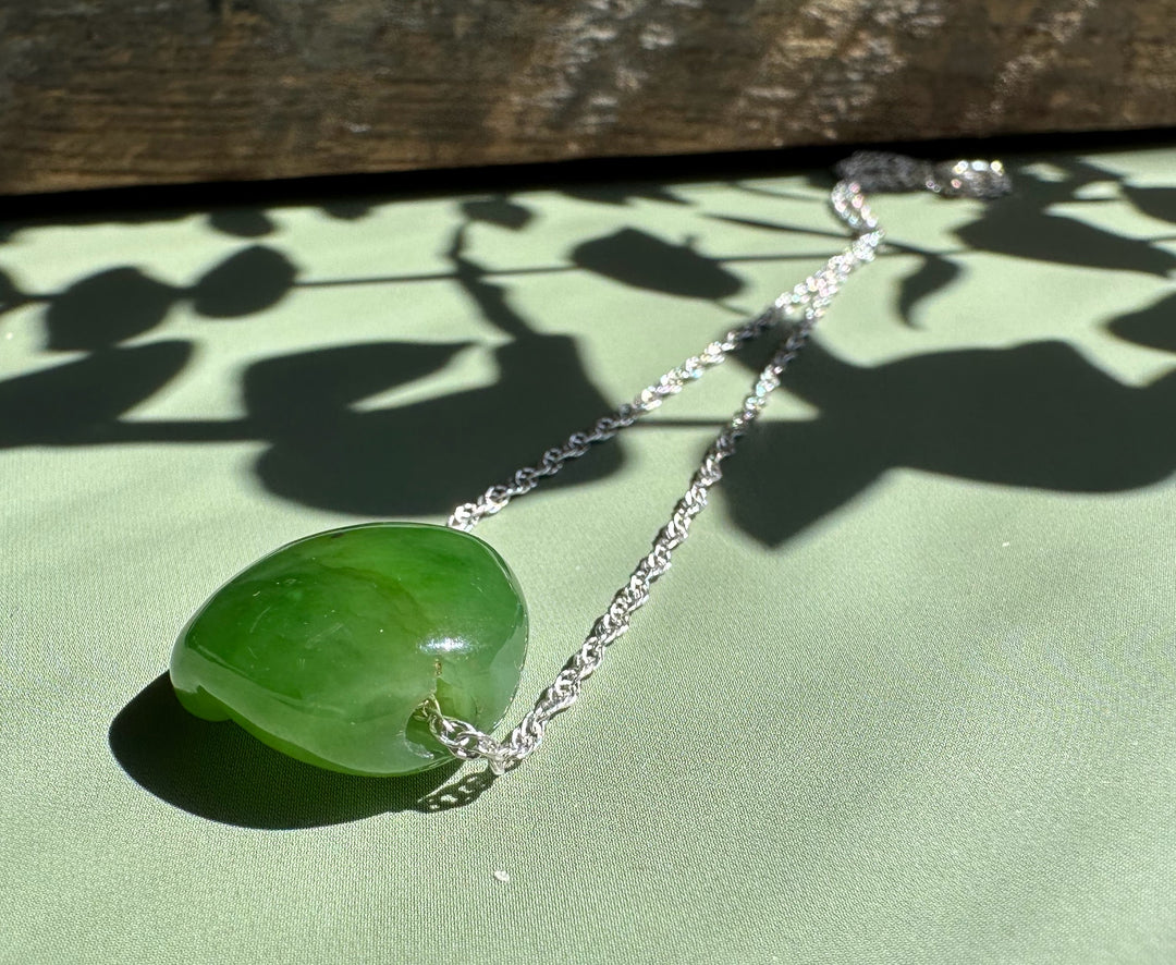 Green jade cat paw pendant with silver chain on pale green background