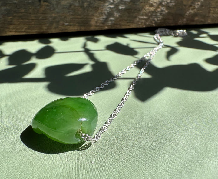 Green jade cat paw pendant with silver chain on pale green background