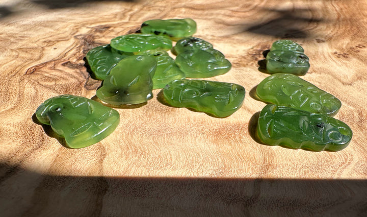 Eleven green jade tiki pendants with carved faces spread on a wooden surface
