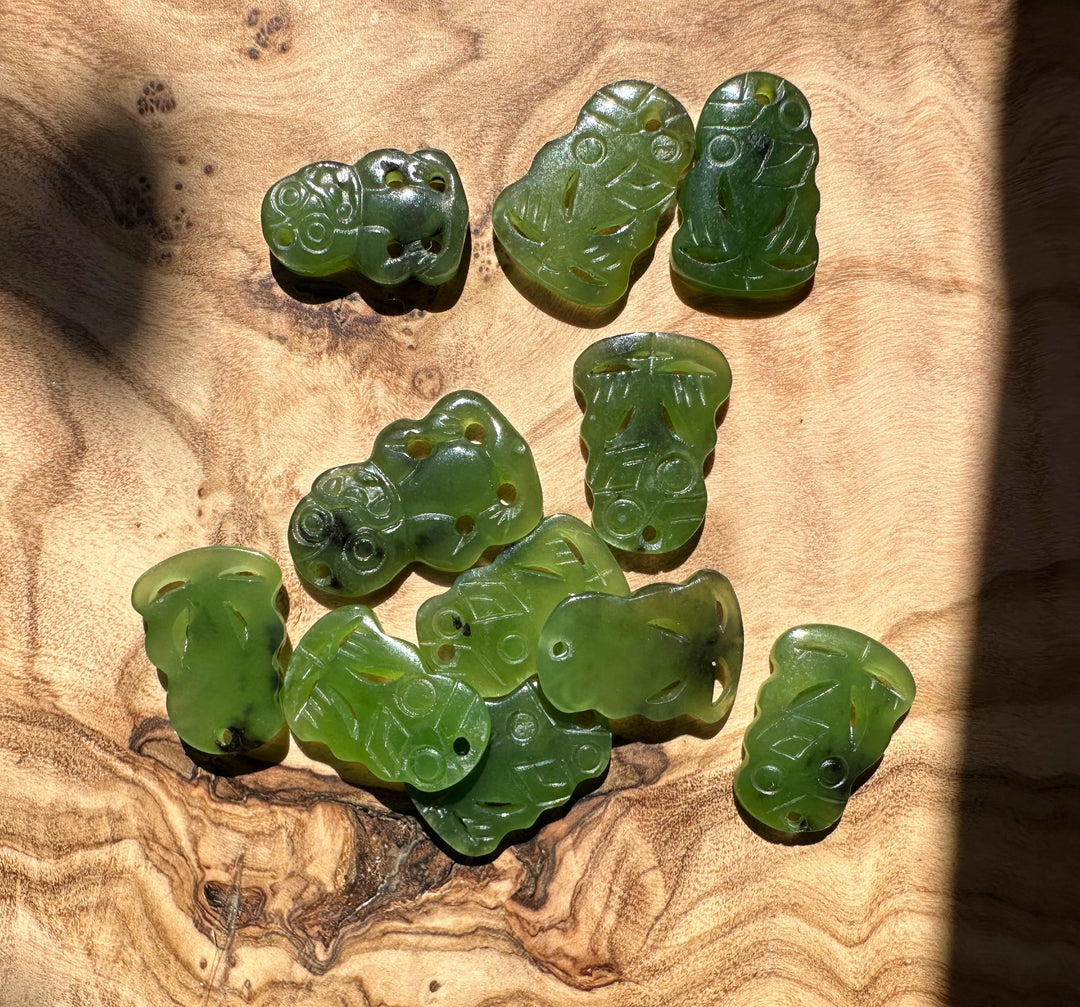 Several green jade tiki pendants with carved features and holes scattered on wood