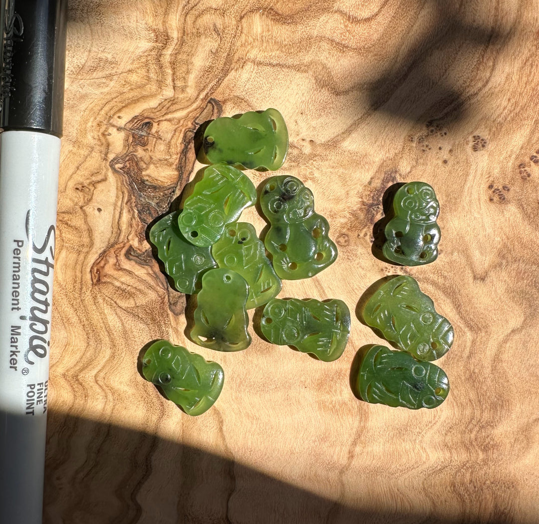 Vintage set of eleven small green jade tiki pendants scattered on a wooden surface