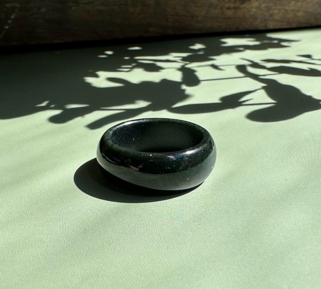 Polished black nephrite jade wide band ring resting on a pale green surface with leaf shadows