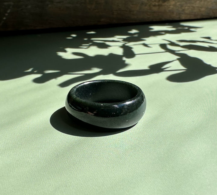 Polished black nephrite jade wide band ring resting on a pale green surface with leaf shadows