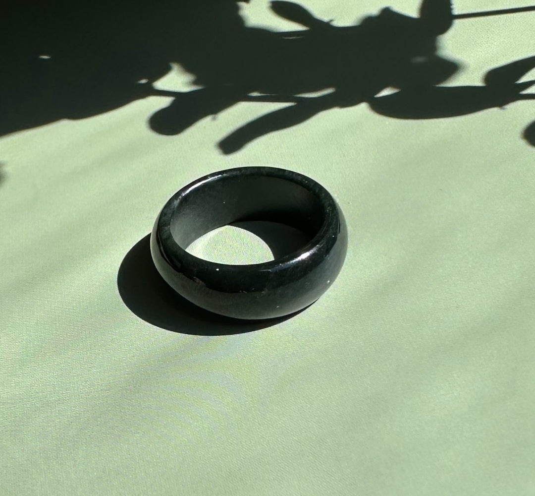 Dark green nephrite jade wide band ring on a pale green background with shadow