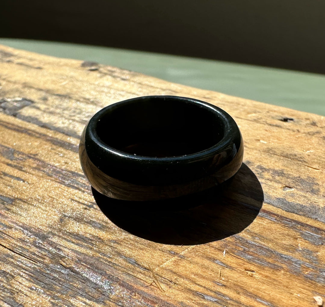 Glossy dark nephrite jade wide band ring resting on a weathered wooden surface outdoors