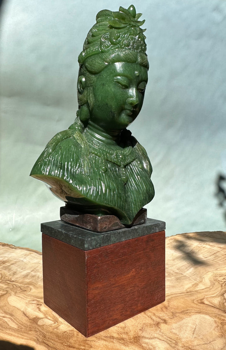 Green Guanyin statue viewed from the side, detailed robe texture and ornate crown on a dark slate top and wooden pedestal.