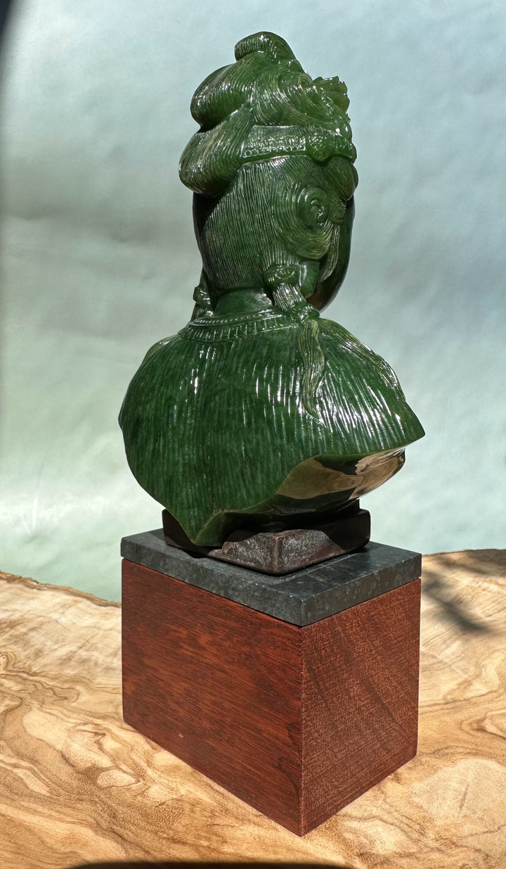 Rear view of green Guanyin statue showing the crown and sculpted hair, mounted on a wooden block base.