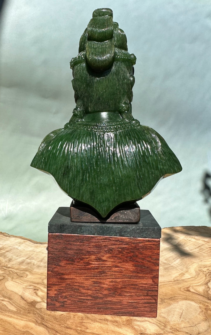 Rear view of a green Guanyin statue with long robes on a two-tier pedestal.