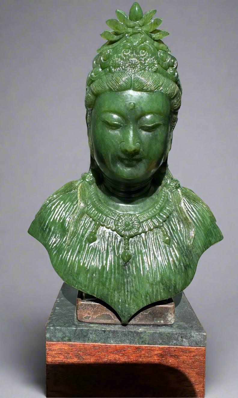 Green jade Guanyin statue bust with ornate crown and necklace atop a dark stone base on a wooden plinth