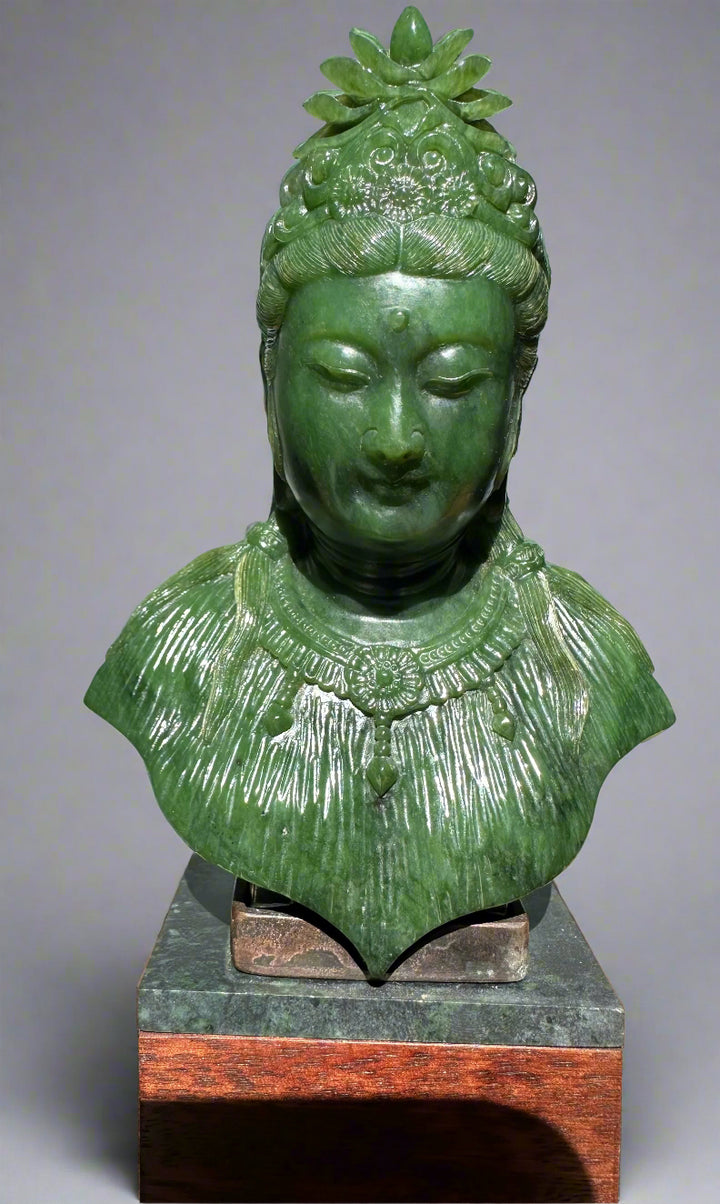 Green jade Guanyin statue bust with ornate crown and necklace atop a dark stone base on a wooden plinth
