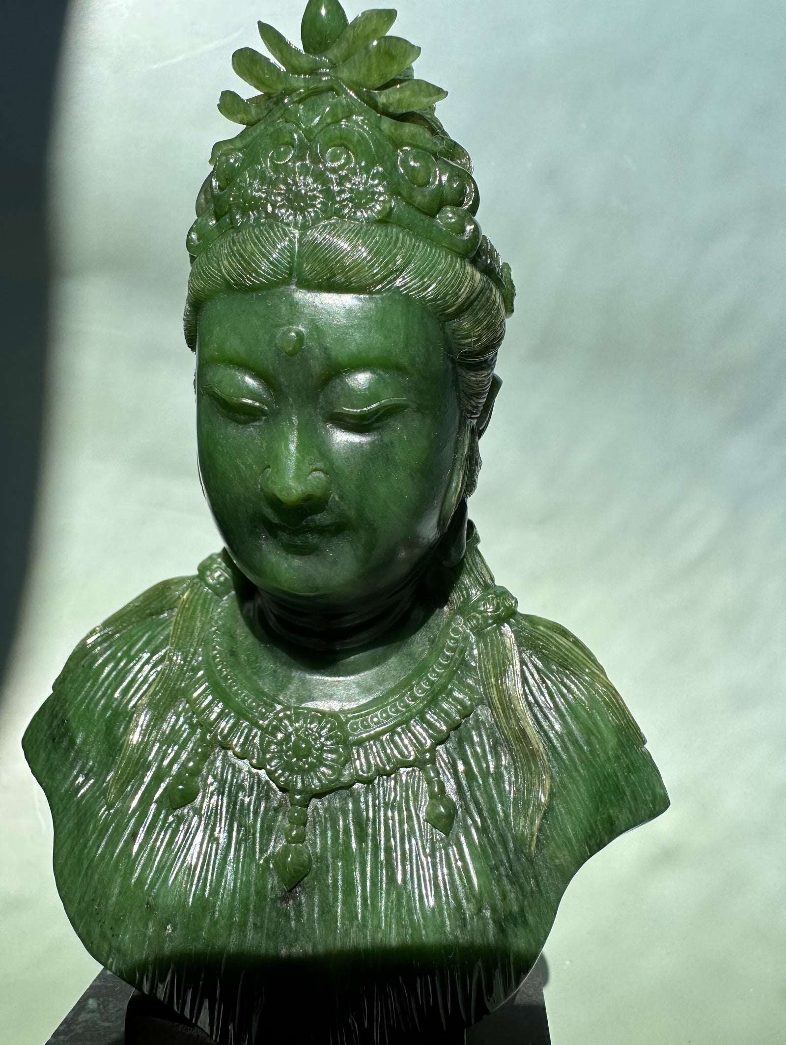 Green Guanyin statue 5 inches with ornate crown and beaded necklace on a dark pedestal.