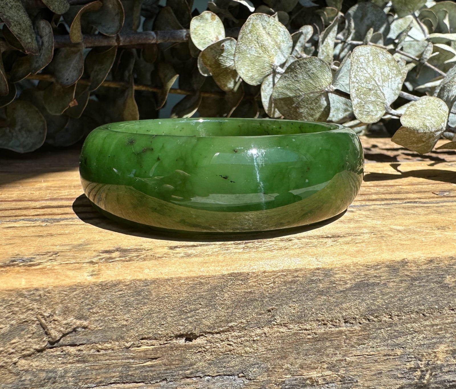 Green jade wide bangle on a weathered wooden surface with eucalyptus leaves in the background