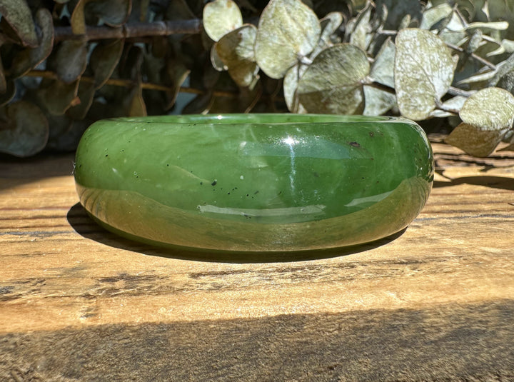 Canadian Jade Wide Bangle on a sunlit wooden surface with a leafy backdrop