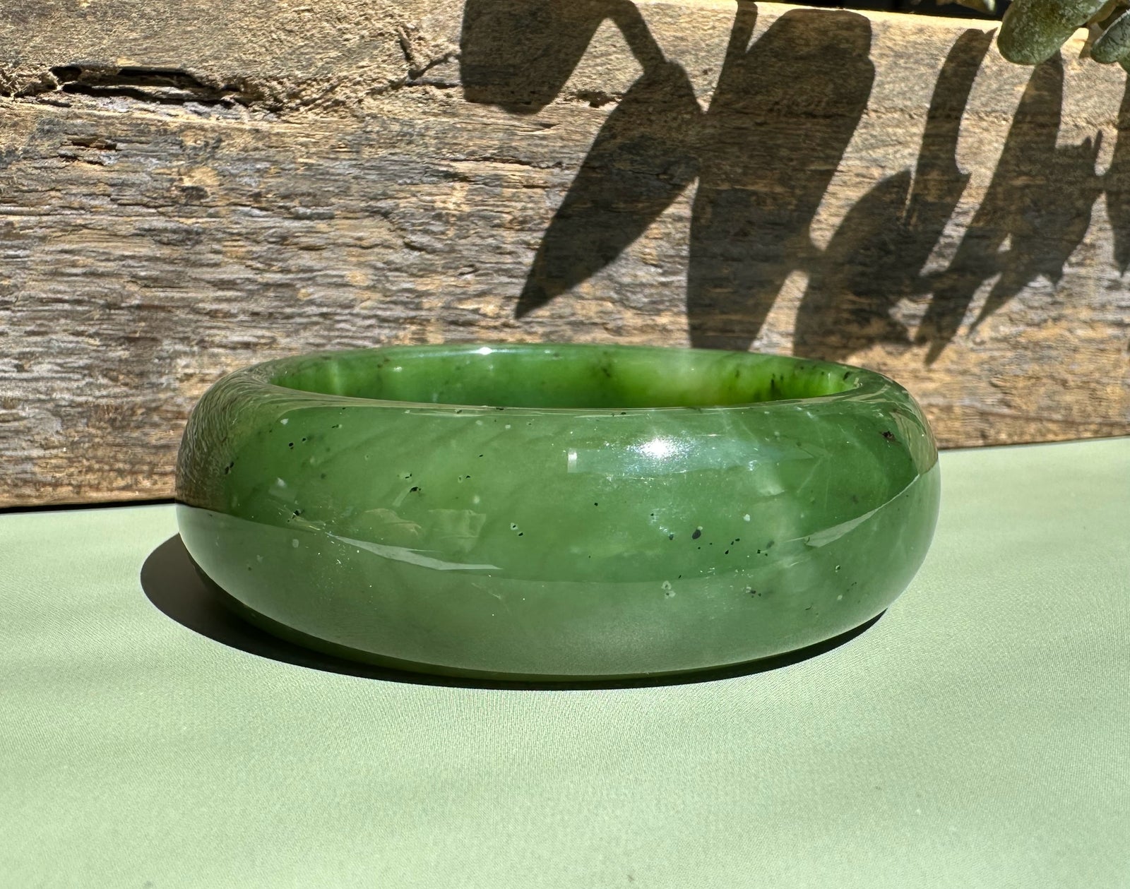 Canadian jade wide bangle in vivid green rests on a wooden surface