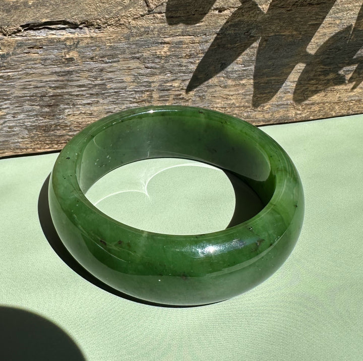 Circular green jade wide bangle on pale green fabric with a rustic wooden backdrop